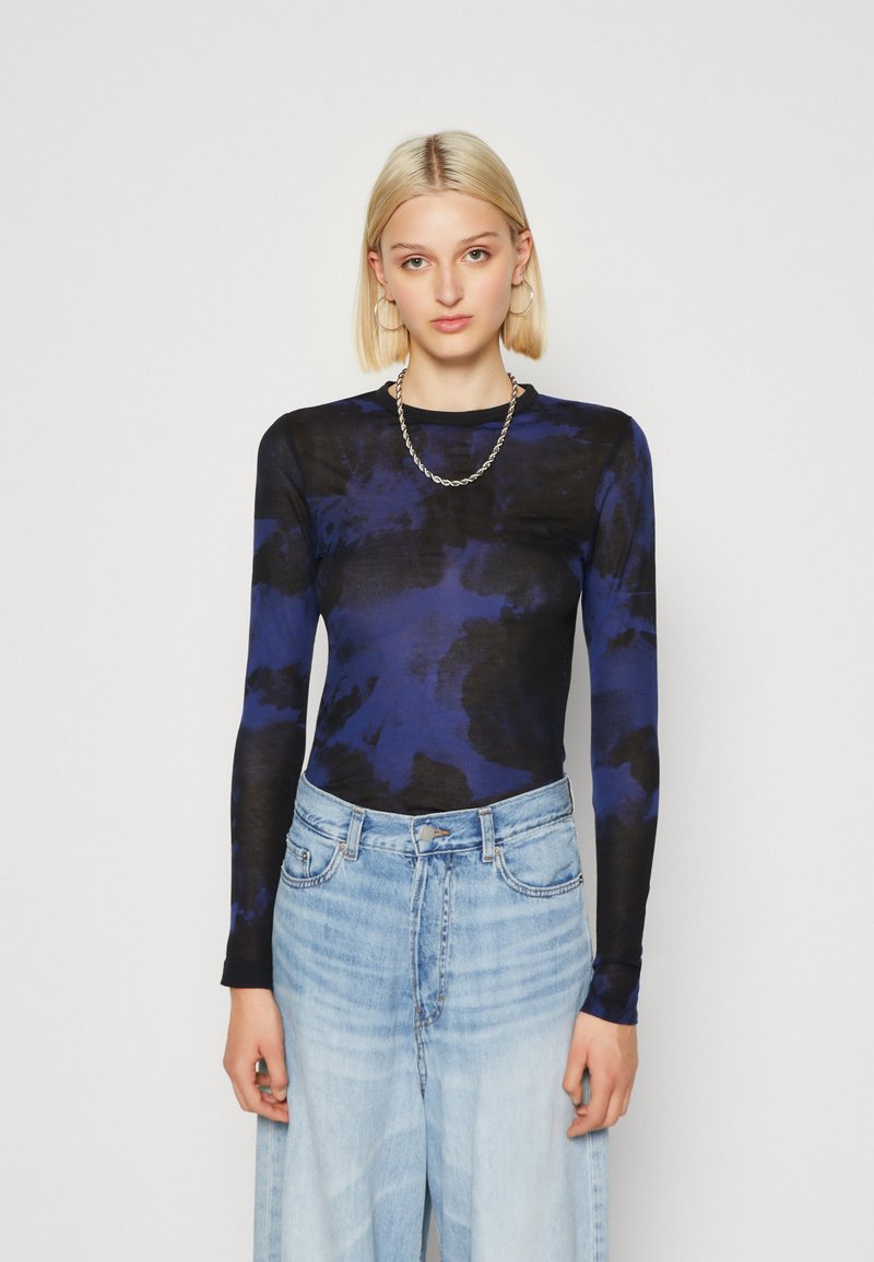 Maglietta a maniche lunghe con un motivo tie-dye blu e nero, realizzata in un tessuto leggero, abbinata a jeans chiari a vita alta.