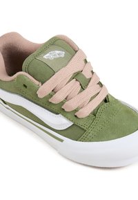 Green canvas sneakers with beige laces, white side stripe, and white rubber sole. Logo featured on padded tongue. Textured upper.