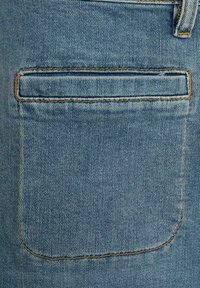 Denimsko blago svetlo modre barve; ima zadnji žep s zaobljenimi robovi in kontrastnim zlatim šivom ob šivu.