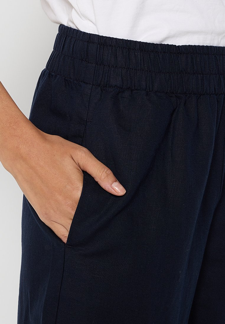 Marineblaue Leinenhosen mit einem elastischen Bund, seitlicher Tasche, glatter Textur und lockerer Passform.