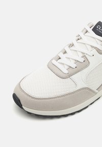 Baskets blanches et grises de sport avec un dessus en mesh, des accents en daim et un système de laçage, avec une semelle extérieure en caoutchouc noir.