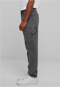 Volné šedé džíny z denimu s bočními kapsami, poutky na opasek a mírně vybledlým povrchem, spárované s bílými teniskami.