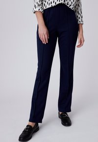 Navy broek met een gladde textuur, voorzien van verticale naaddetails, een getailleerde pasvorm en een hoge tailleband. Gecombineerd met zwarte instappers.