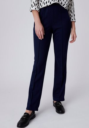Pantalones azul marino con una textura suave, con detalles de costuras verticales, un corte entallado y una cintura alta. Combinados con mocasines negros.