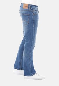 Pantalones de mezclilla acampanados en azul con un lavado claro, que cuentan con dos bolsillos traseros, una etiqueta de cuero marrón en la cinturilla y un corte recto hasta los puños.
