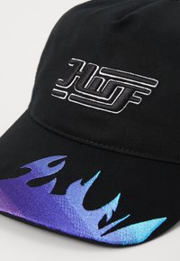 Svart caps med et brodert logo og et gradient design av lilla-blå flammer på skjermen, laget av glatt stoff.