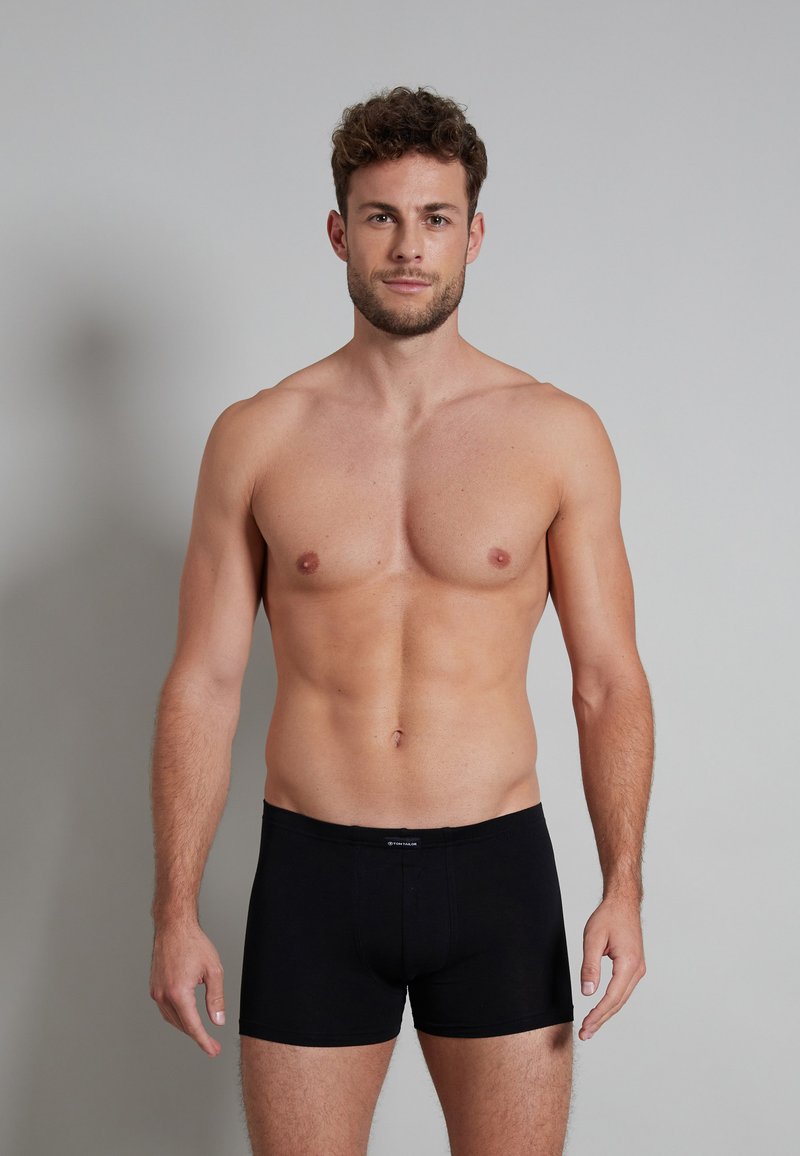 Boxer in cotone nero con una vestibilità aderente, dotati di un cinturino con marchio. Il modello è senza camicia, mostrando chiaramente il prodotto.