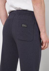 Grijze sweatpants hebben een elastische tailleband, een achterzak met een zwart label en een zachte, gestructureerde stof.
