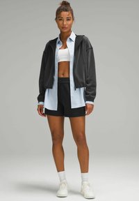 Black cropped hoodie, light blue button-up shirt, white sports bra, black shorts, and white sneakers. Casual athletic style with layered design.