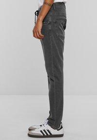 Szürke farmernadrág, tapered fit fazonban, húzózsinóros derékkal és oldalsó zsebekkel, fehér sneakers cipőkkel párosítva.