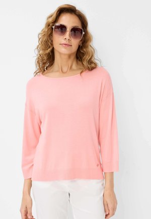 Pull léger rose avec un large col bateau, des manches trois-quarts et une coupe décontractée, associé à de grandes lunettes de soleil.