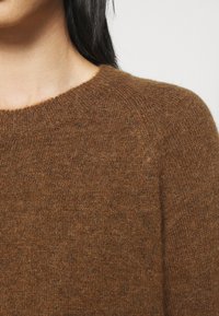 Suéter marrón hecho de un suave tejido de punto, con un escote redondo y un acabado texturizado. La toma en primer plano muestra su cálido tono y fino patrón.
