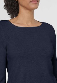 Marineblaues Strickoberteil mit weitem Ausschnitt und langen Ärmeln. Der Stoff wirkt weich mit einer glatten Textur und subtilem Nahtdetail entlang der Säume.