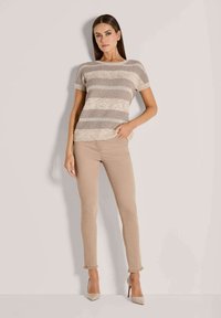 Gehaakt gestreept shirt in beige en taupe met korte mouwen, gecombineerd met aansluitende beige broek met rafelige zoom, en beige hoge hakken.