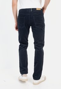 Marineblauwe corduroy broeken met een rechte pasvorm, voorzien van twee achterzakken en een leren label op de tailleband. G gedragen met witte sneakers.