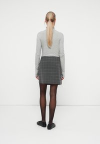 Grå langærmet bluse kombineret med en sort og grå ternet mini-nederdel, sorte strømpebukser og sorte flade sko; glat tekstur og casual design.