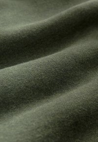 Olivgrüner Stoff mit einer weichen, strukturierten Oberfläche, die sanfte Dehnbarkeit und feine Strickdetails aufweist, erzeugt zarte Wellen und Falten.