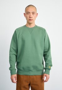 Felpa girocollo verde con polsini e orlo a costine, caratterizzata da una leggera trama. C'è un piccolo logo sul maniche sinistra.