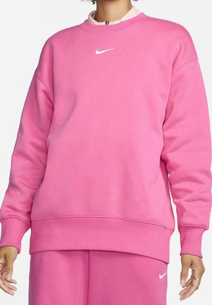 Osoba nosząca różową bluzę Nike i pasujące różowe spodnie z białymi logo Nike na klatce piersiowej i biodrze.