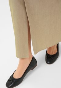 Jupe beige avec une fente latérale, associée à des ballerines en cuir noir à bout rond et à un nœud décoratif. Texture lisse dans l'ensemble.