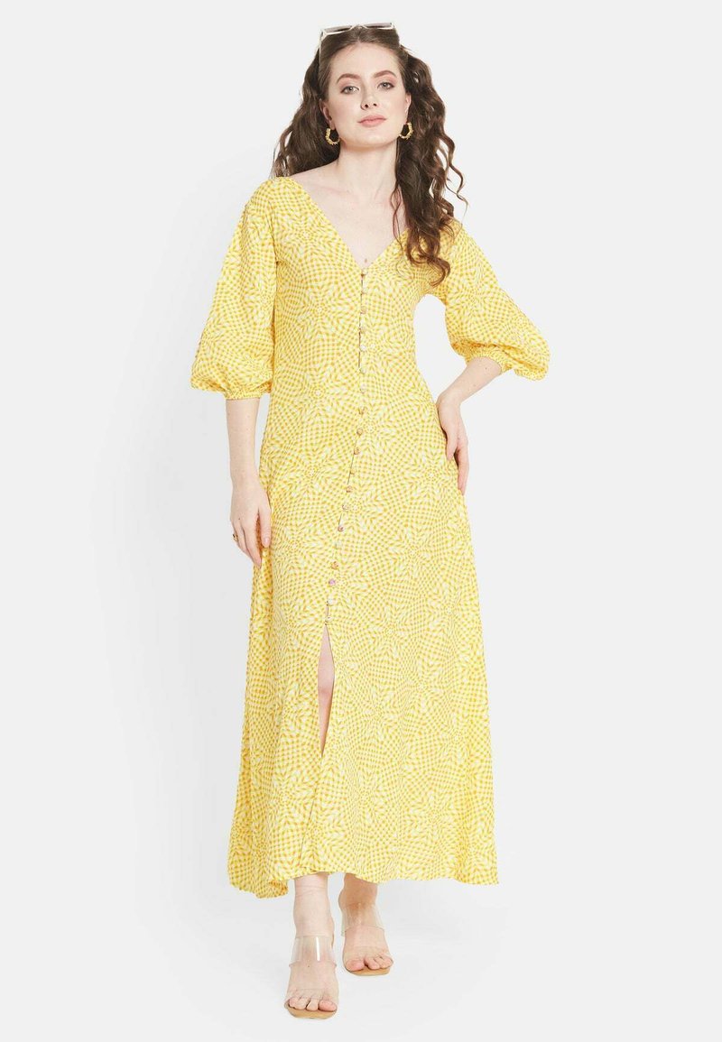 Gelbes, blumiges Maxikleid mit Puffärmeln, Knopfleiste und Schlitzen bis zum Oberschenkel. Hergestellt aus leichtem, strukturiertem Stoff. Klare Sandalen.