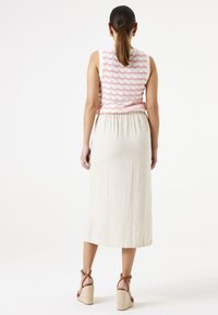 Mouwloos topje met een roze golvend patroon, gecombineerd met een beige enkellange rok. Brown sandalen met hakken met banden maken de look compleet.