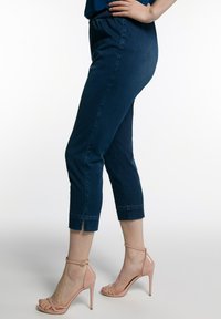 Pantalones capri de mezclilla azul oscuro con cintura elástica, aberturas en los tobillos y corte ajustado, combinados con sandalias de tacón alto de color rosa claro.