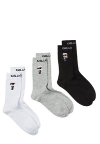 Tři páry ponožek: bílé, šedé a černé. Každý pár nese jméno "Karl Lagerfeld" a karikaturu postavy v slunečních brýlích.