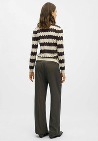 Braun- und cremefarbenes gestricktes Sweatshirt mit Zickzack-Muster und langen Ärmeln, kombiniert mit grauen weiten Hosen und schwarzen Schuhen. Sichtbare gerippte Bündchen.