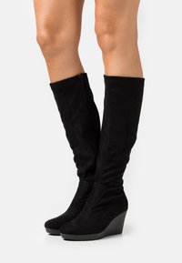 Bottes compensées noires en daim montant au genou, avec un bout rond, une fermeture éclair latérale et une texture lisse, dotées d'une légère plateforme pour plus de hauteur.