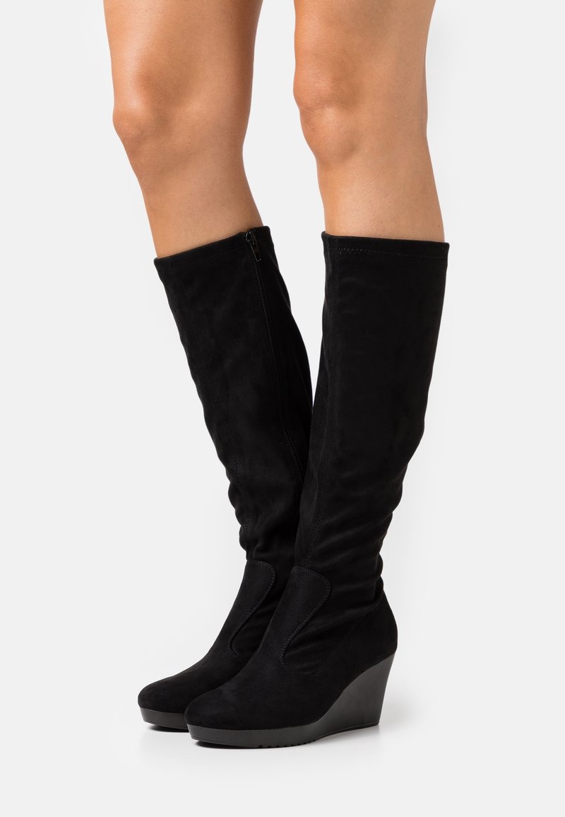Bottes compensées noires en daim montant au genou, avec un bout rond, une fermeture éclair latérale et une texture lisse, dotées d'une légère plateforme pour plus de hauteur.