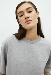 Graues Baumwoll-T-Shirt mit kurzen Ärmeln, Rundhals-Ausschnitt, lässiger Passform und leichter Textur. Glattes Material mit minimalen Details.