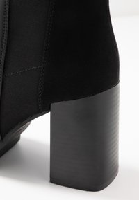 Mustat nilkkurit, joissa on tyylikäs muotoilu, sileä mokkamateriaali, pyöreä korkea korko ja joustavat sivupaneelit. Minimalistinen ja moderni ilme.