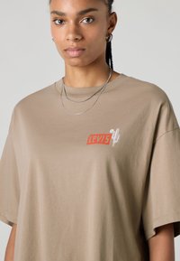 Beige cotton t-shirt featuring a red "Levi's" logo and cactus graphic. Relaxed fit with short sleeves and a round neckline.