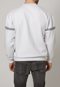 Bílá fleecová mikina s kulatým výstřihem, žebrovanými manžetami a strukturovaným zadním dílem. Má tenké šedé pruhy podél ramen.