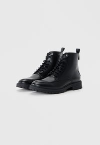 Botas de cuero negro hasta el tobillo con cierre de cordones en la parte delantera, cremallera lateral, punta redonda, suela texturizada y detalles cosidos para mayor durabilidad.