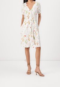 Blommig klänning med korta ärmar, v-ringning och skärp i midjan. Tillverkad av lätt tyg med vit bakgrund och flerfärgade blommönster.