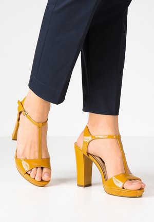 Gule lakerede højhælede sandaler med T-strap design, åben tå og kraftig hæl. Glat tekstur og minimale hardware detaljer.