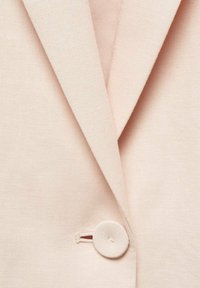 Light pink blazer fabric with a smooth texture, featuring notched lapels, a round button closure, and subtle stitching details.