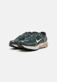 Sapatilhas de corrida em malha verde com uma entressola bege e solado preto. Apresenta um swoosh branco e detalhes texturizados no design superior.