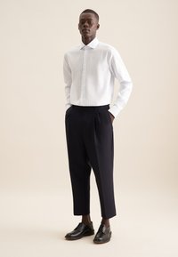 Camicia a righe bianca e azzurro chiaro con colletto classico, abbinata a pantaloni scuri di navy su misura e scarpe di pelle nera.