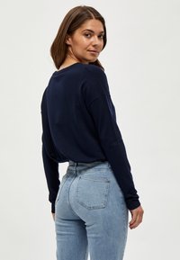 Pull marin avec une coupe décontractée et des poignets côtelés, associé à un jean taille haute bleu clair avec deux poches arrière.