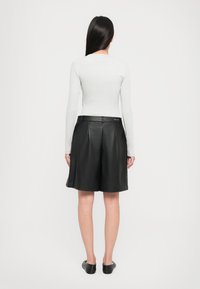 Sorte skinnshorts med plisseringer og høy midje, med beltehanker og glatt tekstur. Modellen har på seg en tettsittende lysegrå topp.