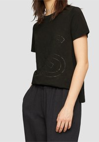 Svart kortärmad t-shirt i mjukt tyg med en tonad logotryck. Kombinerad med löst sittande mörka byxor för en avslappnad look.