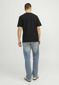 Sort bomulds T-shirt, rund hals, korte ærmer, parret med lyseblå denim jeans. Model set bagfra, iført sandaler. Enkel design.