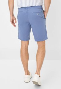 Pantaloni corti azzurri chiari realizzati in tessuto intrecciato, con due tasche posteriori e dettagli dei bottoni a contrasto. Indossati con sneaker bianche per un look casual.