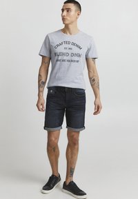 Siva kratka majica s kratkimi rokavi z črnimi napisi, v kombinaciji z dark jeans kratkimi hlačami s zvitimi robovi. Črni športni copati dopolnjujejo oblačila.