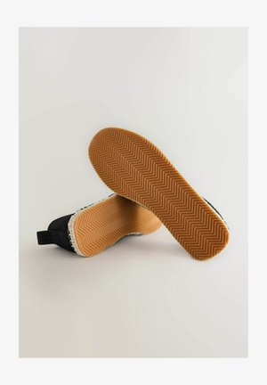 Scarpe slip-on nere in tessuto con suola in gomma a motivo zigzag e bordo in bianco testurizzato a contrasto.