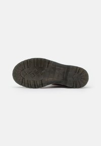 Suela de goma con profundas estrías para tracción, con un patrón texturizado y detalles en relieve. Color oscuro con un diseño robusto y resistente.