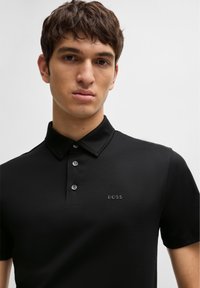Sort polo shirt med krave, prydet med tre knapper. Diskret logo på brystet, glat tekstur og korte ærmer.